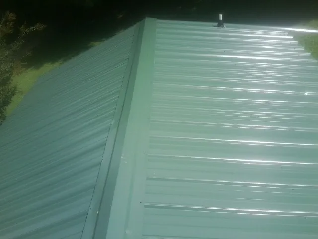 New green metal panels meeting at the ridge of a roof — Flat Roof Repair work by our crew in Osceola